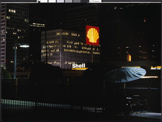 A color photograph of a city at night from a hotel roof with a Shell gas station sign lit up.