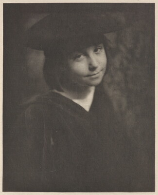 A black-and-white portrait photograph of a smiling, young White girl wearing a black hat and a black dress.