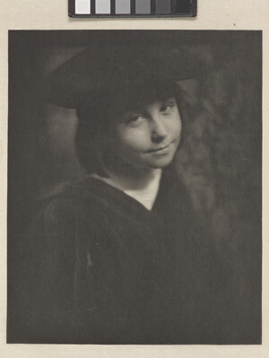 A black-and-white portrait photograph of a smiling, young White girl wearing a black hat and a black dress.
