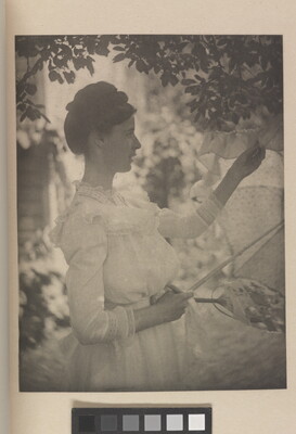A soft-focus, black-and-white photograph of a White woman in profile wearing a white long-sleeved dress holding a white parasol under a tree.