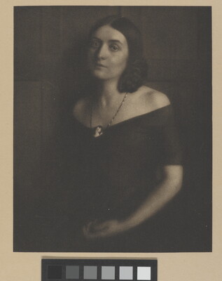 A sepia-toned portrait photograph of a young White woman wearing an off-the-shoulder dress and a cameo necklace.