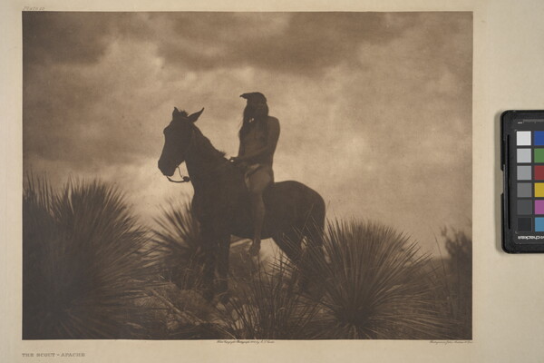 A sepia-toned photograph of an Indigenous person sitting atop a horse surrounded by yuccas; the low light makes the figures look almost like silhouettes.
