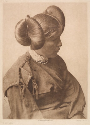 A sepia-toned portrait photograph of a young, Indigenous girl wearing a cultural hairstyle and a long sleeved dress.