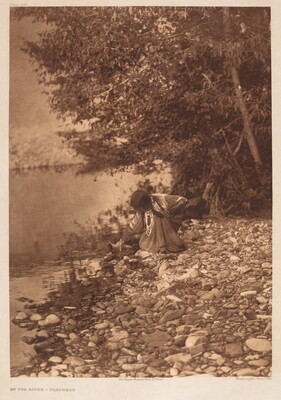 A sepia-toned photograph of an Indigenous woman bending down to pick something up from along a rocky shore.