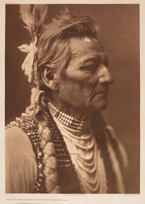 A sepia-toned portrait photograph of a Native American man in profile from the shoulders up wearing traditional dress.