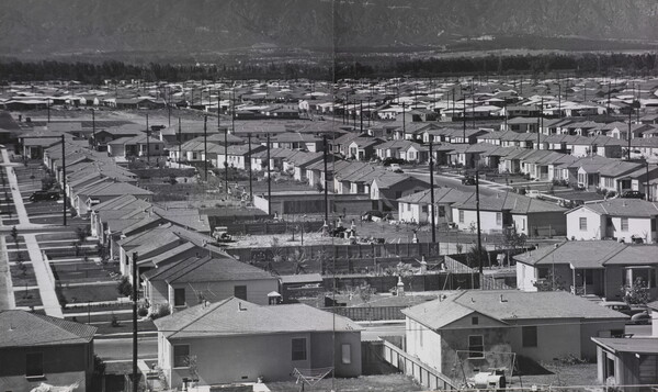 A black-and-white photograph of a sprawling suburb of ranch-style houses with mountains in the distance.