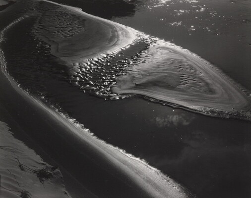 A black-and-white abstract photograph of water washing up on a sandy beach.