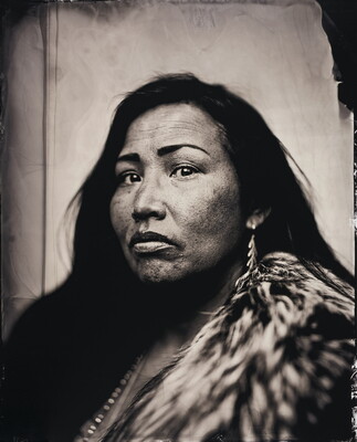 A black-and-white portrait photograph of a Native American woman wearing a fur and long traditional earrings.