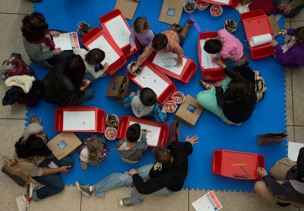 View from above of children and adults sitting on a floor creating art.