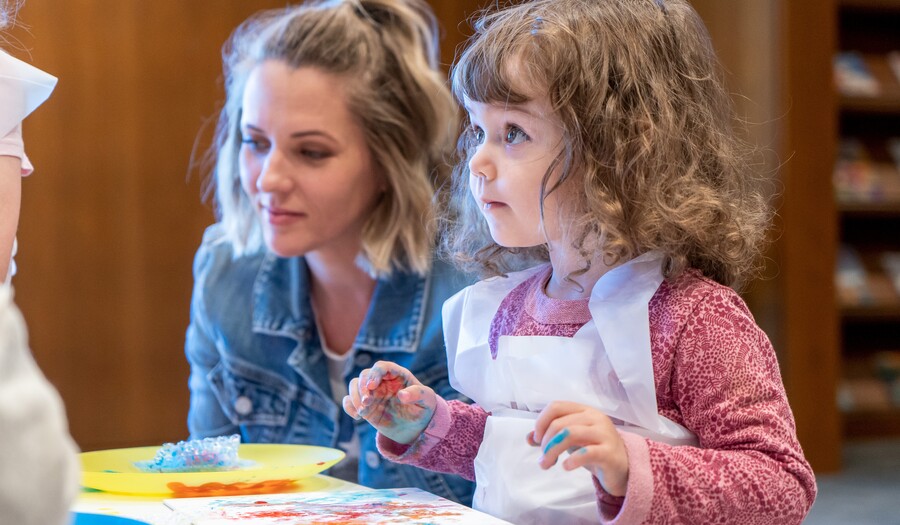 A toddler with paint-covered hands and an adult make art at a table.
