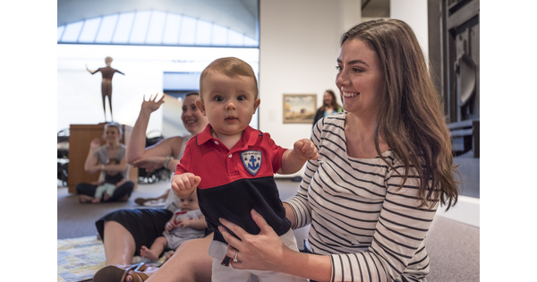A smiling woman holds her standing baby in a Carter gallery.