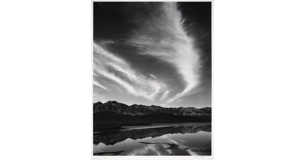 A black-and-white landscape photograph of mountains and clouds that reflect on the still water in the foreground.