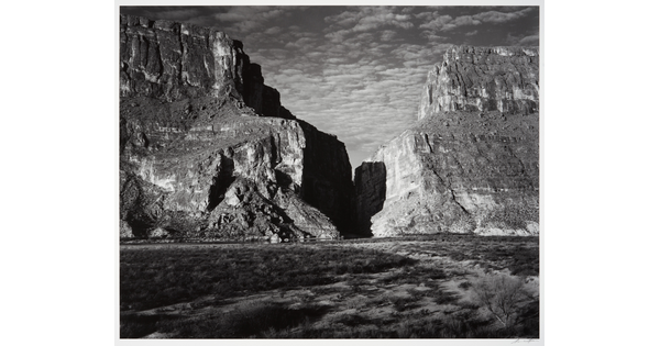 A black-and-white photograph of a canyon between two large mountains.
