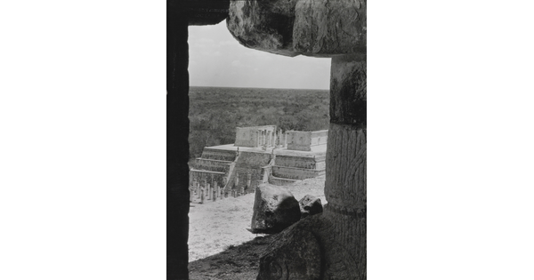 A black-and-white photograph of an ancient step pyramid viewed through a stone window.