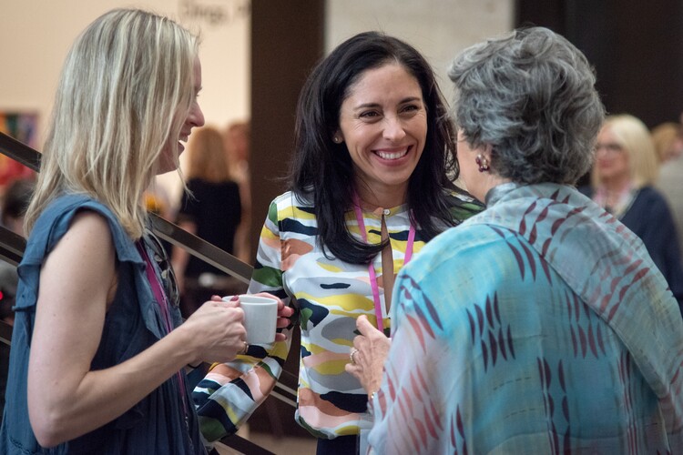 Three women stand talking and laughing