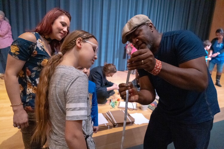 A Carter Community Artist shows a measuring tape to a girl and a woman