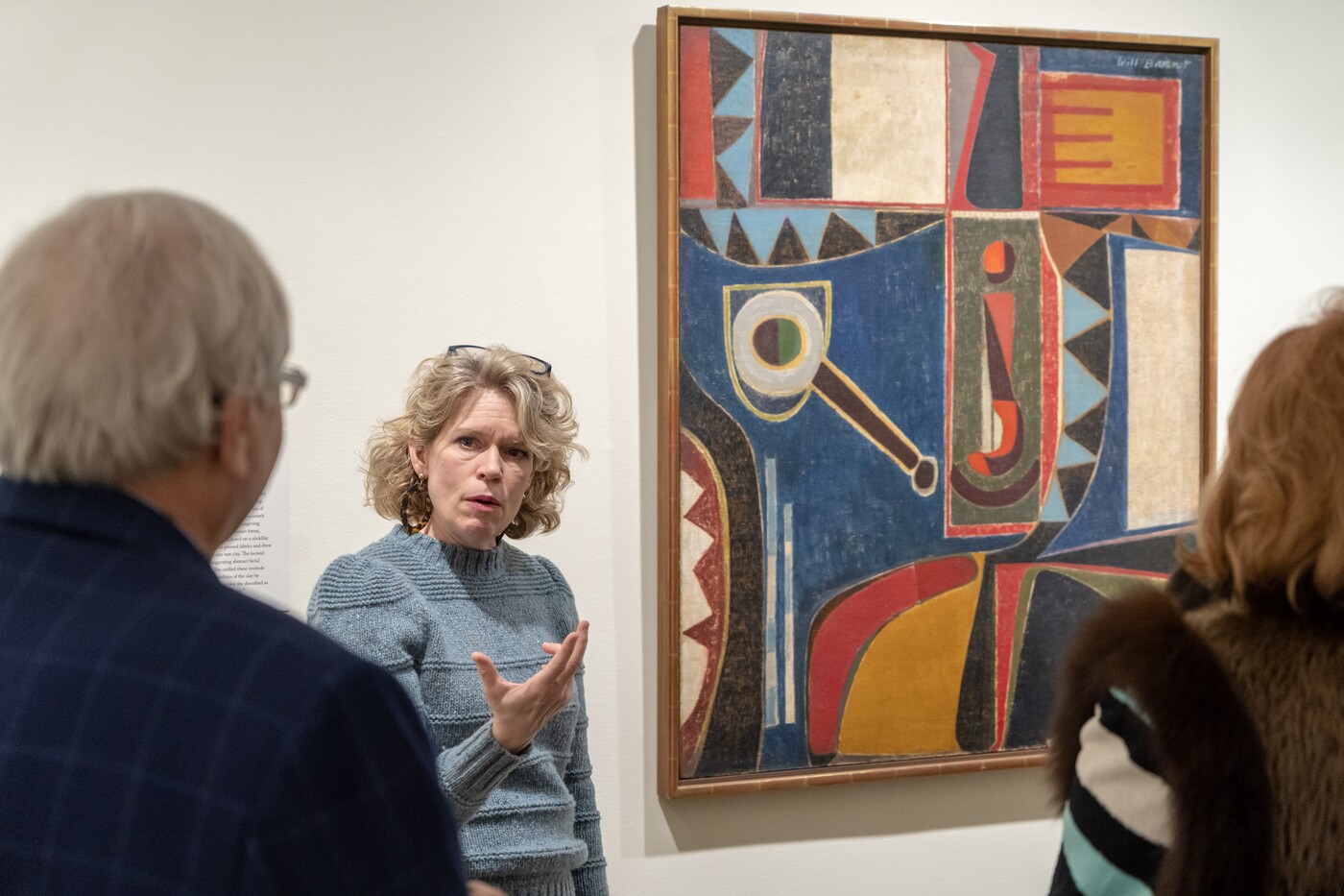 Woman talking to guests in front of Will Barnet's Self-Portrait