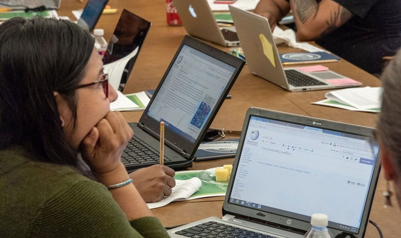 Group sits at table with laptops and research materials