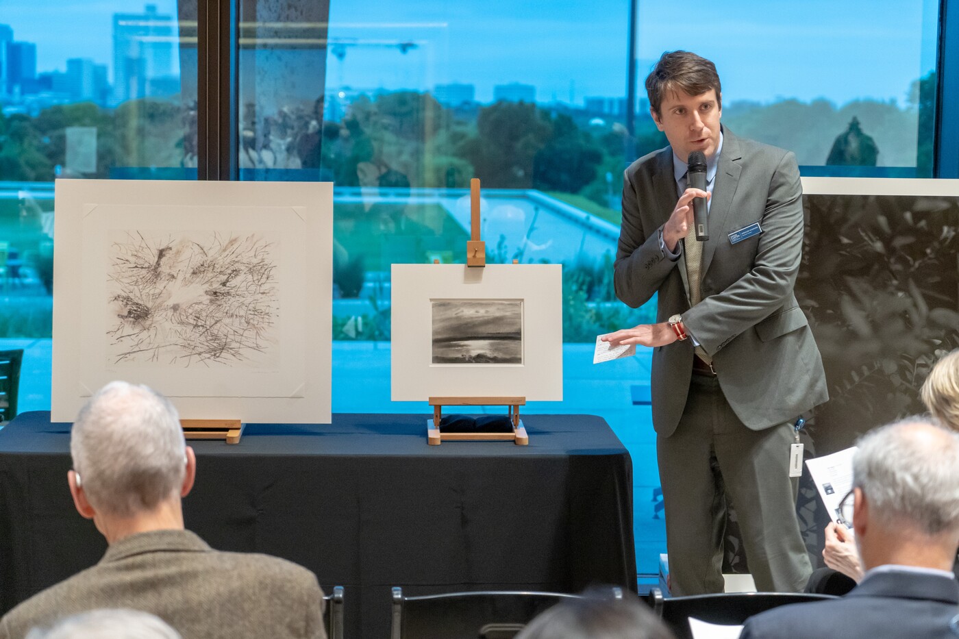 Man stands in front of three artworks gesturing toward them
