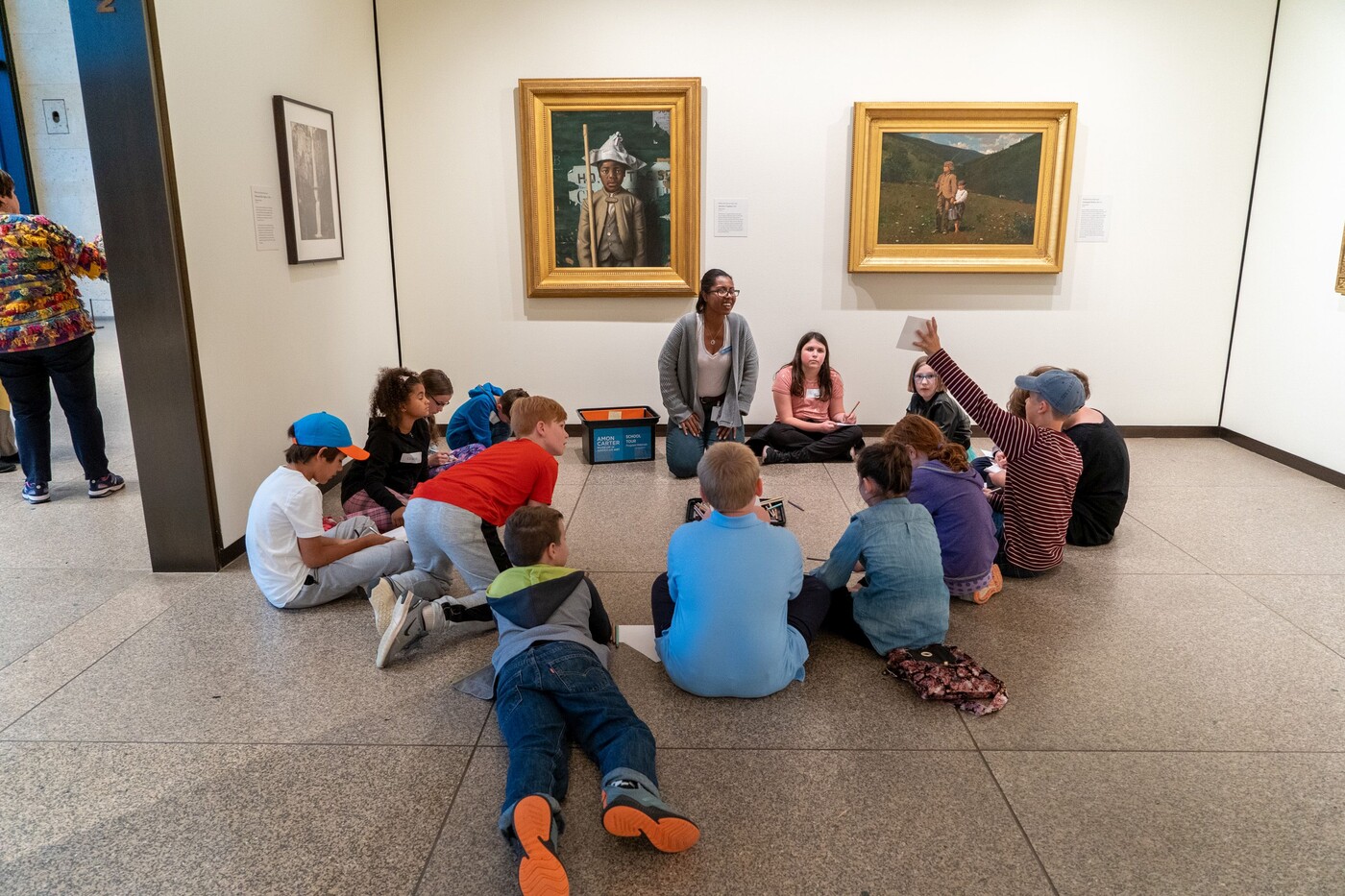 Group of children lays and sits on the floor of a gallery with paintings