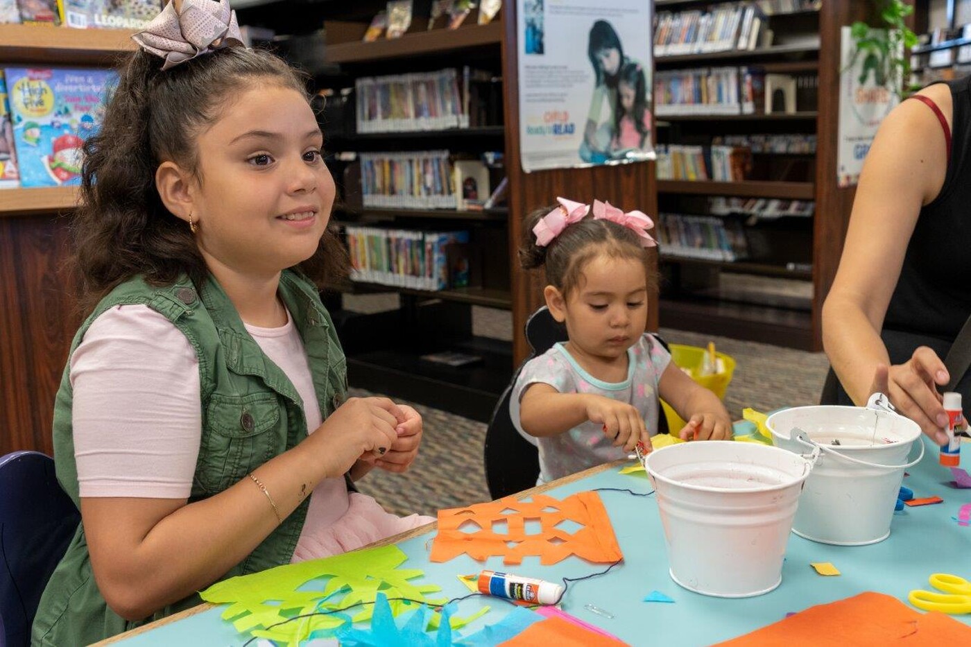 Two children sit at a table strewn with art supplies; they are each working on their own projects
