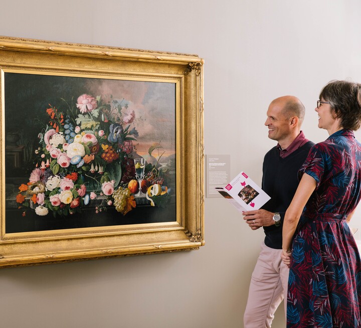 Couple look at a still life painting; the man holds a museum guide in his hands