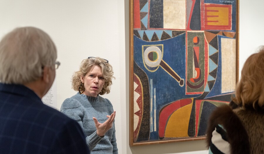 A curator talks to guests in front of Will Barnet's "Self-Portrait"