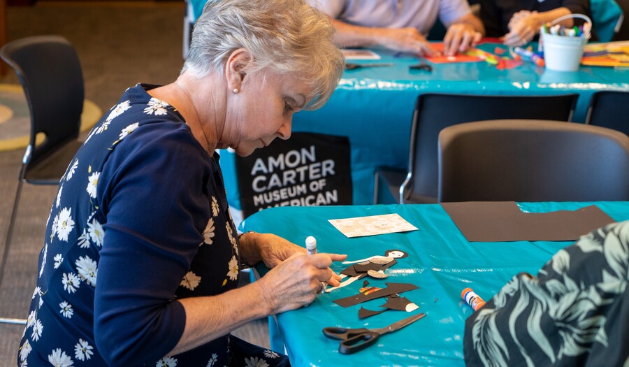 A woman sits at a table and works on a craft