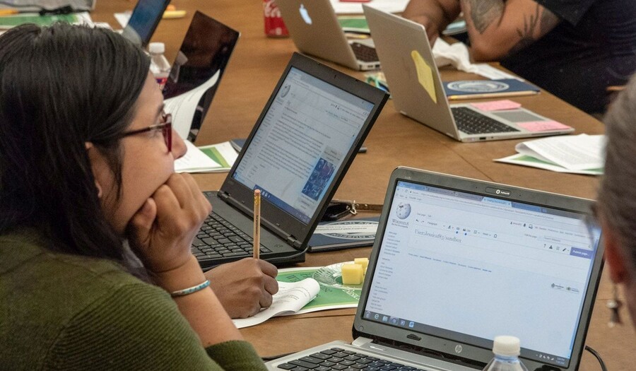 Group sits at table with laptops and research materials