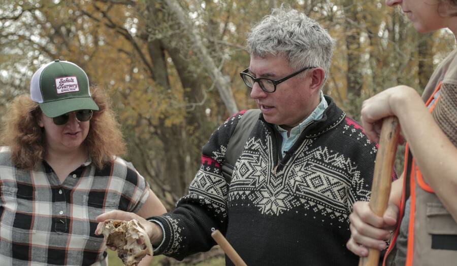 Three people looking at skull with trees behind