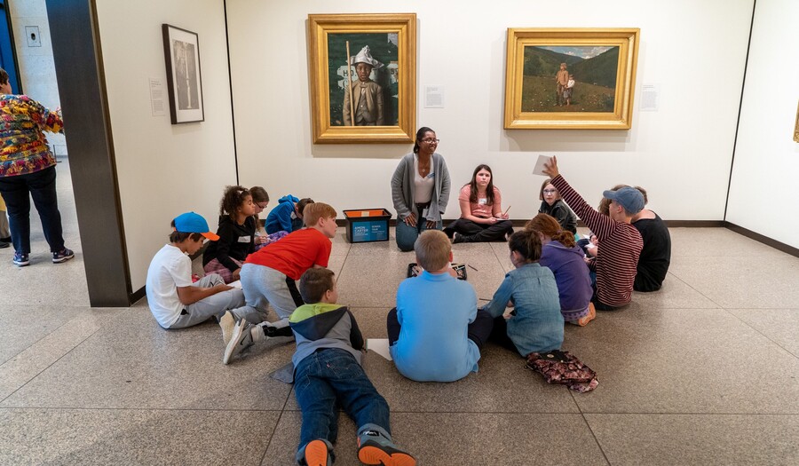 Group of children lays and sits on the floor of a gallery with paintings