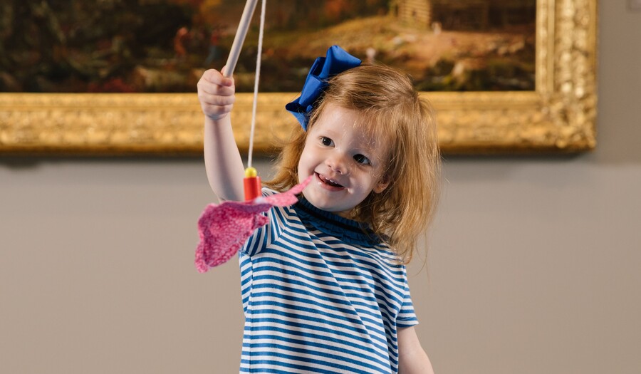little girl catching a toy fish with a stick in front of a painting