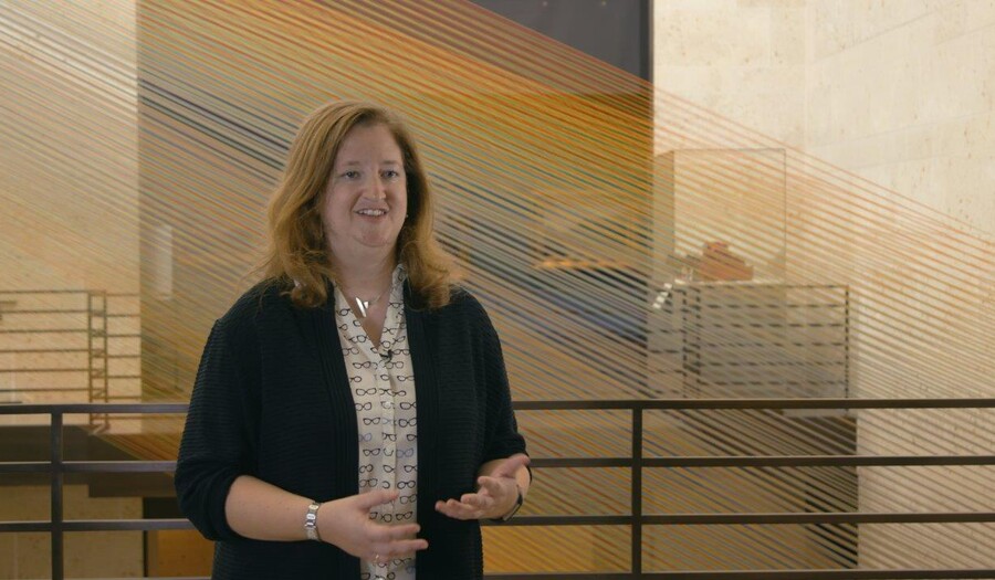 Woman with auburn hair gestures in front of an art installation made from thread.