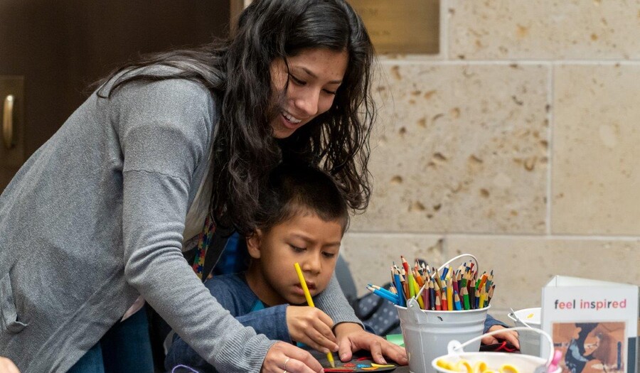 A woman leans over a small child who is sitting at a table working on an art project