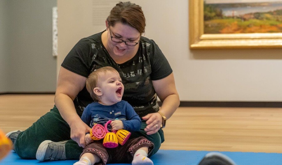 A woman sits on the floor and holds a laughing baby in her lap