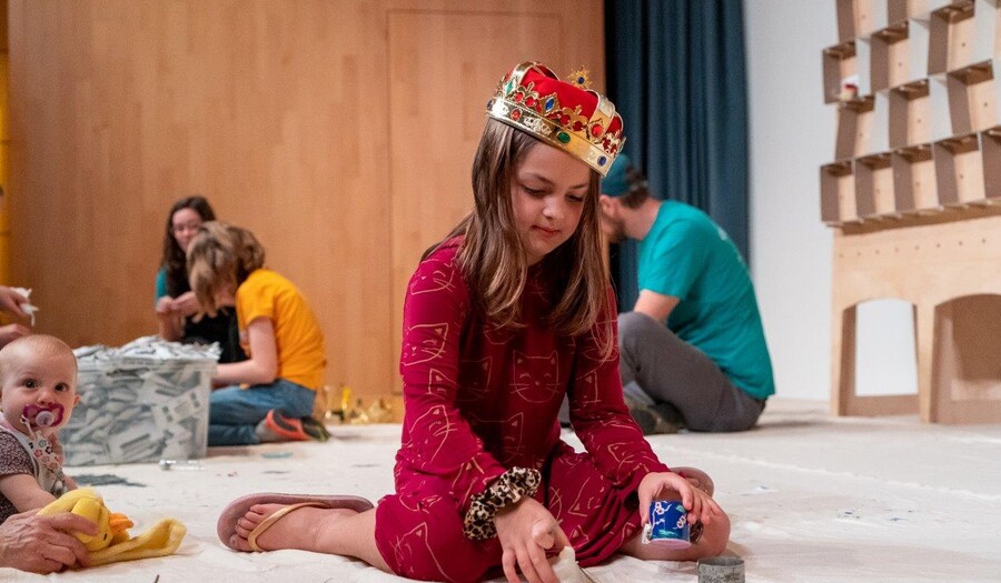 A girl sits on the floor and holds art supplies in her hands
