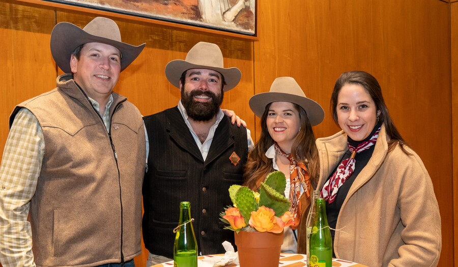 Four light-skinned people stand around a table; all except the person on the far right wear cowboy hats