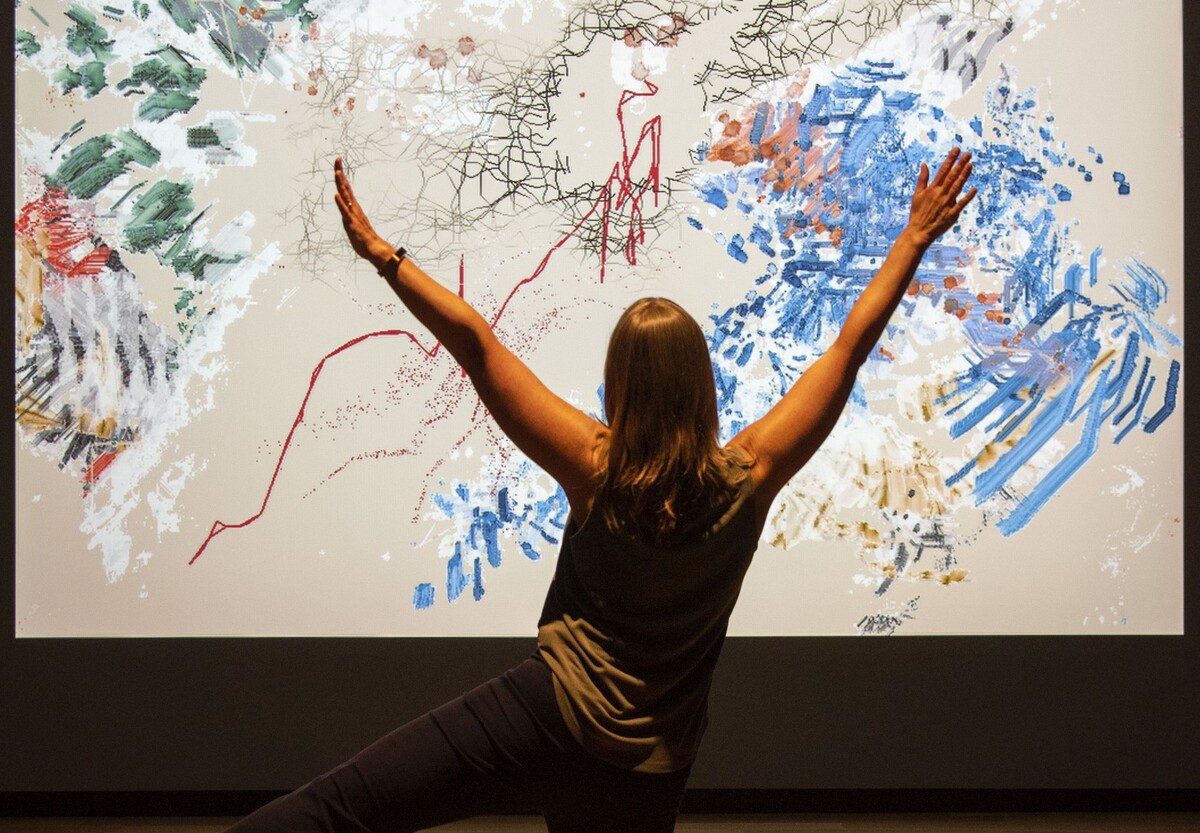 Woman standing with arms and leg raised in front of screen